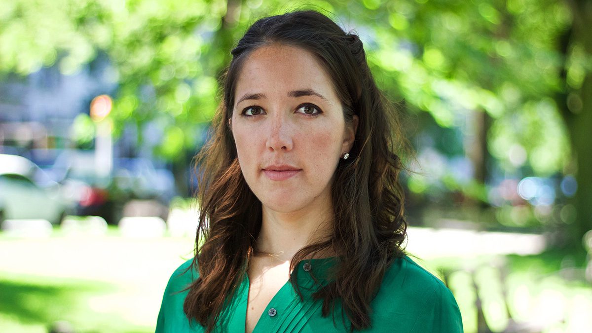 Erin Banco wearing a green shirt and standing outside with trees in the background.